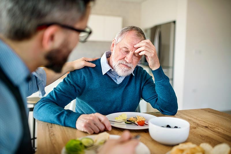 Senior man holding head at dinner table