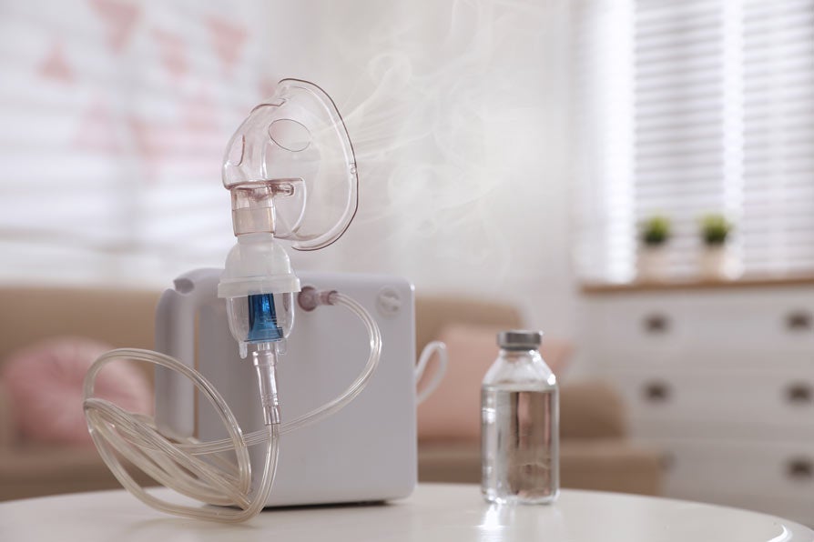 Modern nebulizer with face mask on white table indoors