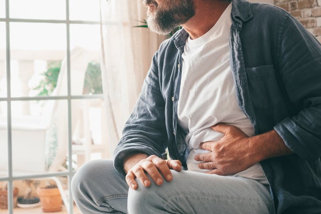 Man holding hand over his stomach while sitting at home