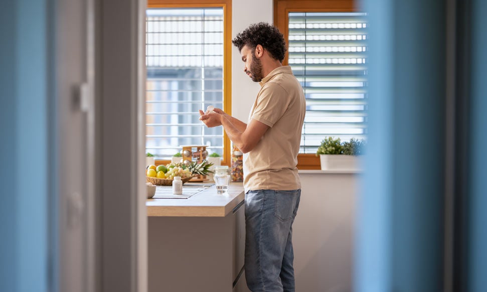 Young man in kitchen at home taking medication