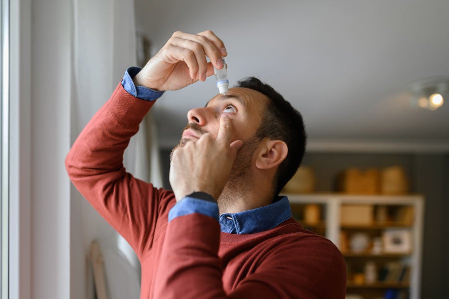 Man in red sweater using eyedrops