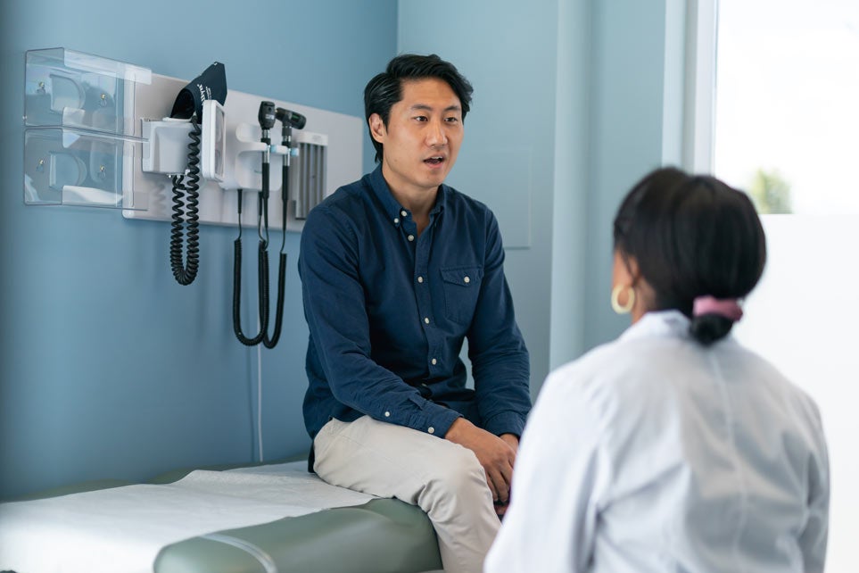 A Korean man is at a routine medical appointment in an exam room talking with the doctor.